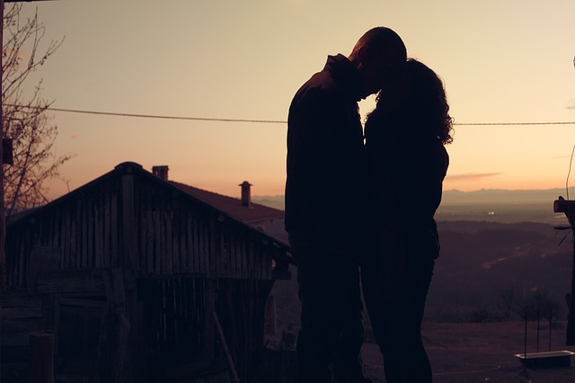 Západ slunce, přítmí, romantika, dva lidi, kteří se k sobě vinou u staré dřevěné stodoly